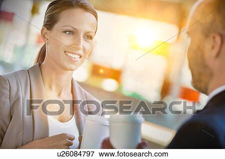 Stock Photo - Portrait of businessman and businesswoman holding cup of coffee while talking and waiting for the train. Fotosearch