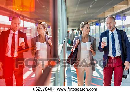 Stock Photo - Portrait of businessman and businesswoman holding cup of coffee while walking and talking . Fotosearch