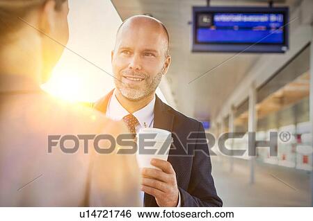 Stock Photograph - Portrait of businessman and businesswoman holding cup of coffee while talking and waiting for the train. Fotosearch