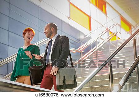 Stock Photograph - Portrait of businessman and businesswoman talking while walking down stairs. Fotosearch