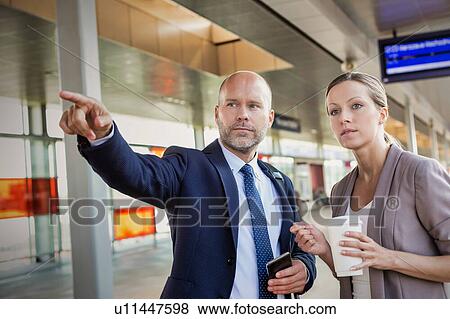 Stock Photo - Portrait of businessman gesturing while talking to young attractive businesswoman in train station. Fotosearch