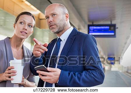 Stock Photo - Portrait of businessman gesturing while talking to young attractive businesswoman in train station. Fotosearch