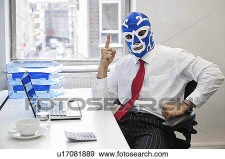 Stock Photo - Portrait of businessman in wrestling mask points up at office desk. Fotosearch