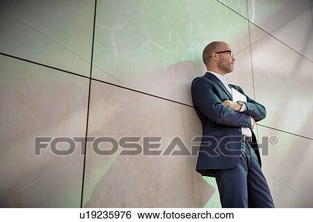 Portrait of businessman standing with arms crossed while leaning on wall View Large Photo Image Stock Photograph - Portrait of businessman standing with arms crossed while leaning on wall. Fotosearch