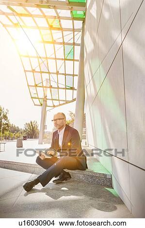 Picture - Portrait of businessman using digital tablet while sitting outside the office. Fotosearch