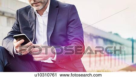 Stock Image - Portrait of businessman using digital tablet while sitting outside the office. Fotosearch