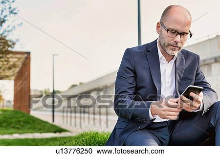 Stock Image - Portrait of businessman using digital tablet while sitting outside the office. Fotosearch