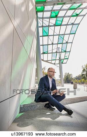 Stock Image - Portrait of businessman using digital tablet while sitting outside the office. Fotosearch
