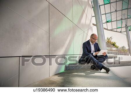 Portrait of businessman using digital tablet while sitting outside the office View Large Photo Image Stock Image - Portrait of businessman using digital tablet while sitting outside the office. Fotosearch