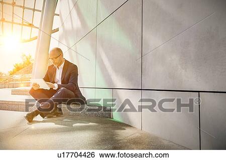 Stock Photograph - Portrait of businessman using digital tablet while sitting outside the office. Fotosearch