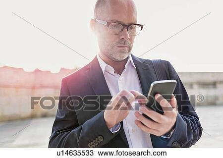 Portrait of businessman using smartphone while leaning on wall View Large Photo Image Stock Image - Portrait of businessman using smartphone while leaning on wall. Fotosearch