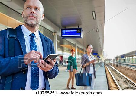 Portrait of businessman using smartphone while waiting for the train in station View Large Photo Image Stock Image - Portrait of businessman using smartphone while waiting for the train in station. Fotosearch