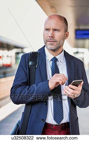 Stock Image - Portrait of businessman using smartphone while waiting for the train in station. Fotosearch