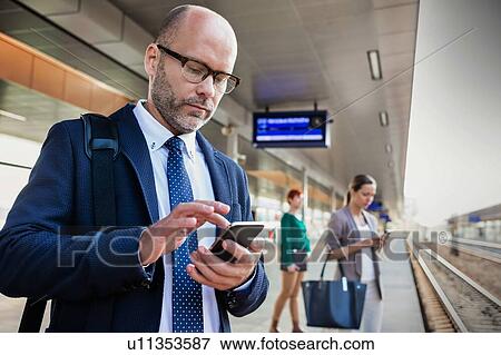 Stock Photo - Portrait of businessman using smartphone while waiting for the train in station. Fotosearch