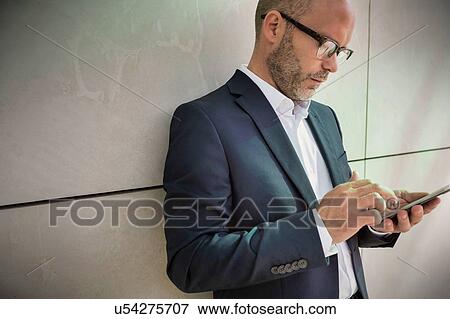 Portrait of businessman using smartphone while leaning on wall View Large Photo Image Stock Photo - Portrait of businessman using smartphone while leaning on wall. Fotosearch