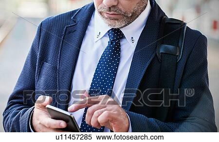 Stock Photography - Portrait of businessman using smartphone while waiting for the train in station. Fotosearch