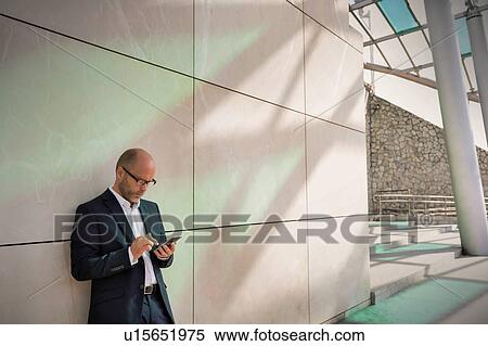 Portrait of businessman using smartphone while leaning on wall View Large Photo Image Stock Photography - Portrait of businessman using smartphone while leaning on wall. Fotosearch