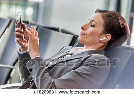 Portrait of businesswoman listening to music on smartphone while waiting for boarding in airport View Large Photo Image Stock Image - Portrait of businesswoman listening to music on smartphone while waiting for boarding in airport. Fotosearch