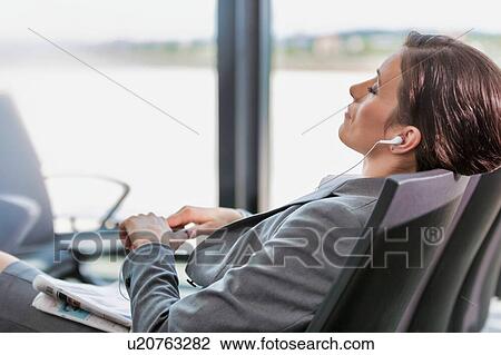 Stock Image - Portrait of businesswoman listening to music on smartphone while sleeping and waiting for boarding in airport. Fotosearch
