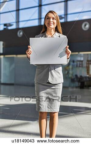 Stock Image - Portrait of businesswoman standing while holding blank white board in arrival area at airport. Fotosearch