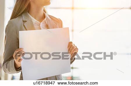 Stock Photo - Portrait of businesswoman standing while holding blank white board in arrival area at airport. Fotosearch