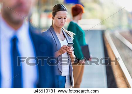 Stock Image - Portrait of businesswoman using smartphone while waiting for the train in station. Fotosearch