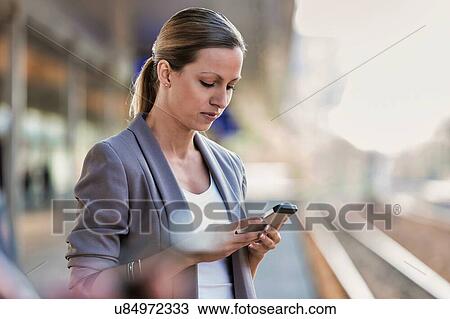 Stock Image - Portrait of businesswoman using smartphone while waiting for the train in station. Fotosearch