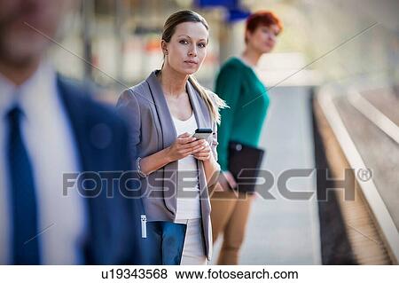 Stock Photo - Portrait of businesswoman using smartphone while waiting for the train in station. Fotosearch
