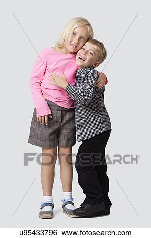 Stock Photograph - Portrait of cheerful young boy embracing sister over white background. Fotosearch
