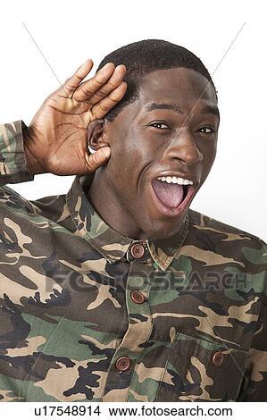 Picture - Portrait of cheerful young military soldier in camouflage clothing with hand behind his ear against white background. Fotosearch