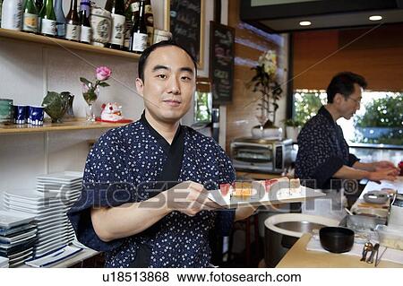 Portrait of chef holding sushi tray with coworker in background View Large Photo Image Stock Photo - Portrait of chef holding sushi tray with coworker in background. Fotosearch