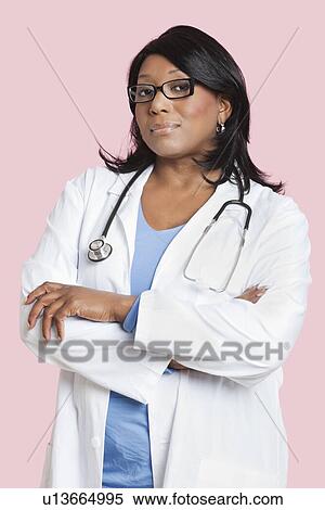 Stock Photography - Portrait of confident mixed race female surgeon over pink background. Fotosearch