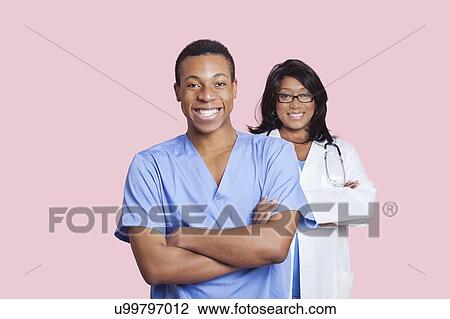 Stock Image - Portrait of confident mixed race male and female surgeons over pink background. Fotosearch