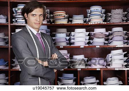 Stock Photo - Portrait of confident owner with arms crossed standing against display cabinet. Fotosearch