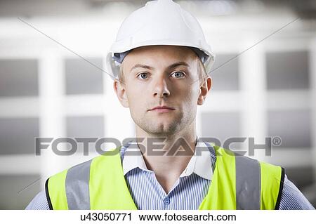 Stock Image - Portrait of confident young architect in hard hat and safety vest. Fotosearch