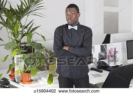 Portrait of confident young businessman standing at office View Large Photo Image Stock Image - Portrait of confident young businessman standing at office. Fotosearch
