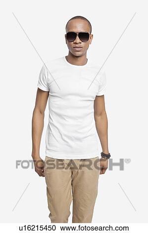Stock Image - Portrait of confident young man wearing sunglasses against white background. Fotosearch