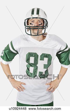 Stock Photo - Portrait of confident young man wearing football uniform against gray background. Fotosearch