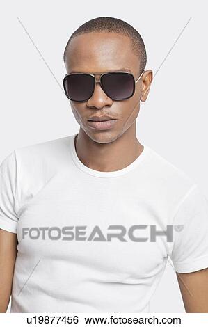 Portrait of confident young man wearing sunglasses against white background View Large Photo Image Stock Photograph - Portrait of confident young man wearing sunglasses against white background. Fotosearch