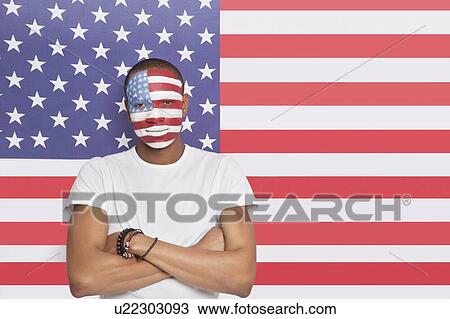 Stock Image - Portrait of confident Young man with painted face against American flag. Fotosearch