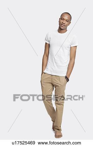 Stock Photo - Portrait of confident young man with hands in pockets against white background. Fotosearch