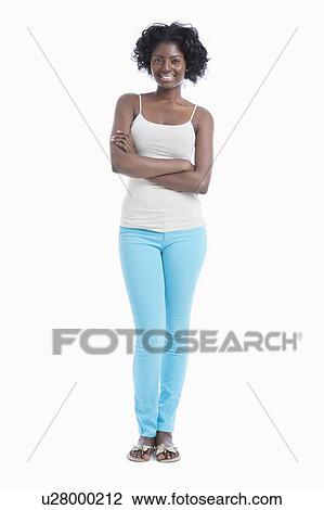 Stock Image - Portrait of confident young woman with arms crossed standing against white background. Fotosearch
