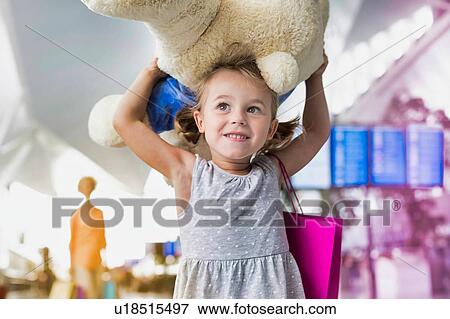 Stock Photo - Portrait of cute little girl carrying her big teddy bear in airport with yellow lens flare. Fotosearch