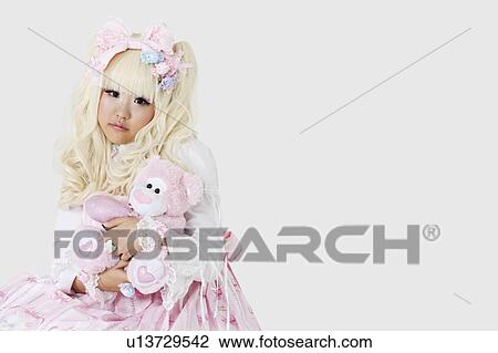 Portrait of cute woman dressed as a doll holding soft toy over gray background View Large Photo Image Stock Image - Portrait of cute woman dressed as a doll holding soft toy over gray background. Fotosearch