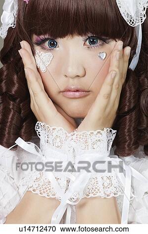 Stock Image - Portrait of cute young woman in doll costume over gray background. Fotosearch
