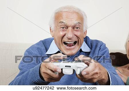 Portrait of excited elderly man playing video game at home View Large Photo Image Stock Image - Portrait of excited elderly man playing video game at home. Fotosearch