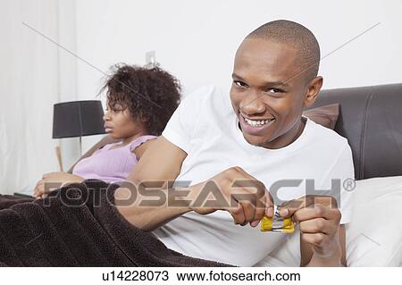 Portrait of excited young man opening condom packet while woman in background View Large Photo Image Stock Image - Portrait of excited young man opening condom packet while woman in background. Fotosearch