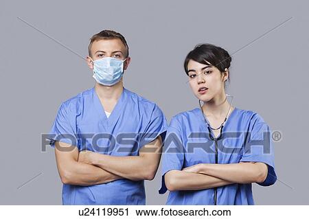 Stock Image - Portrait of female and male surgeons standing with arms crossed over gray background. Fotosearch