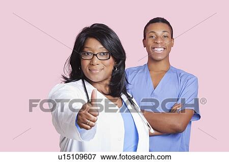 Stock Photo - Portrait of female doctor gesturing thumbs up with male surgeon in the background. Fotosearch