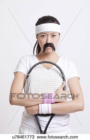 Stock Image - Portrait of female tennis player wearing a fake mustache against white background. Fotosearch